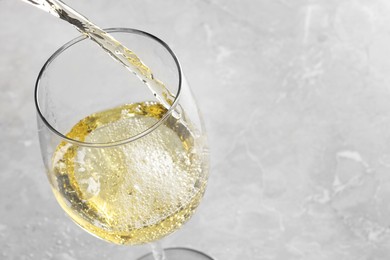 Pouring tasty aromatic wine in glass at gray marble table, closeup. Space for text