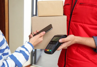 Photo of Woman with smartphone using terminal for delivery payment indoors, closeup