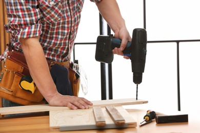 Photo of Young working man using electric drill indoors, closeup. Home repair