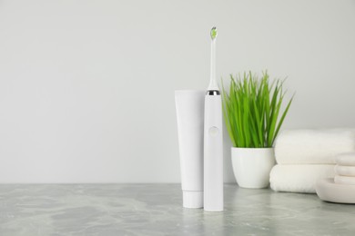 Photo of Electric toothbrush and tube with paste on light grey marble table