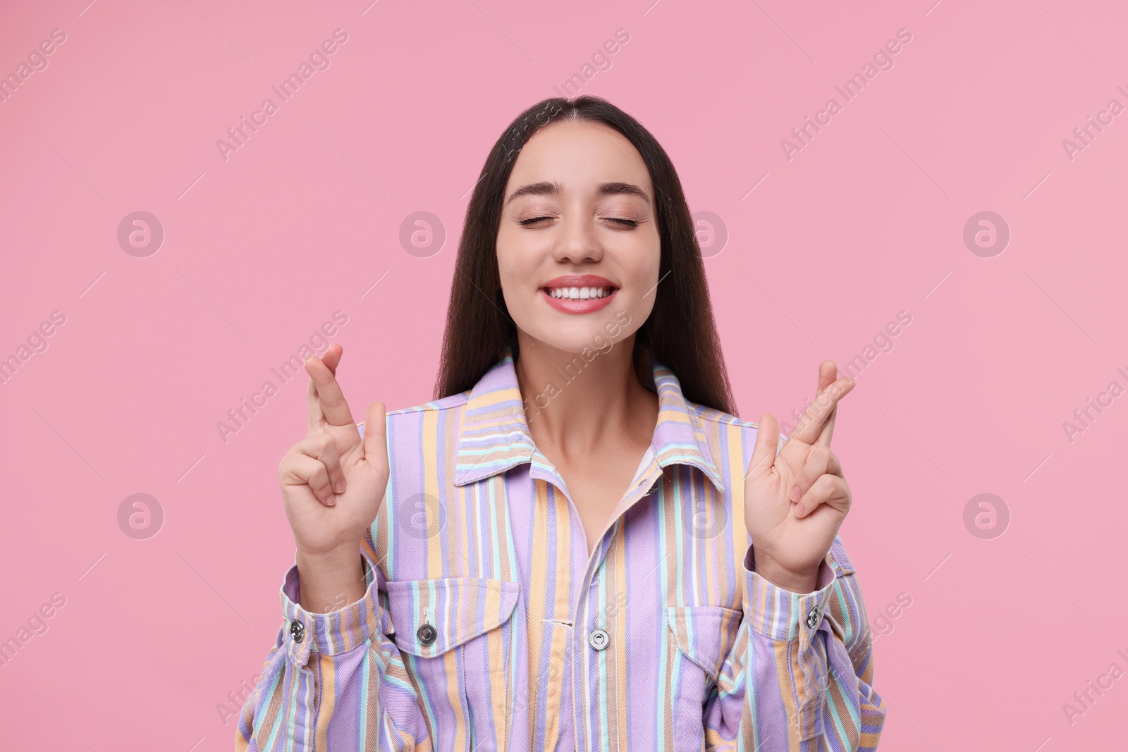 Photo of Happy woman crossing her fingers on pink background