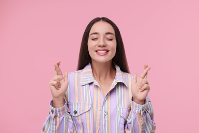 Happy woman crossing her fingers on pink background