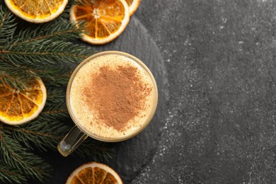 Photo of Glass cup of delicious eggnog with cinnamon and dried orange slices on gray table, flat lay. Space for text