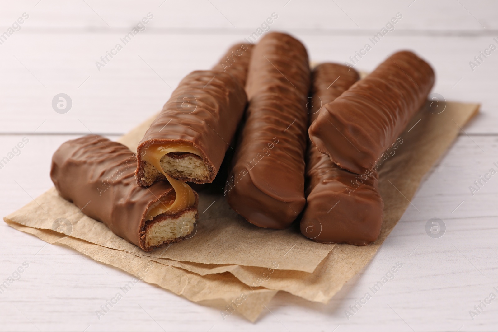 Photo of Tasty chocolate bars with caramel on white wooden table, closeup