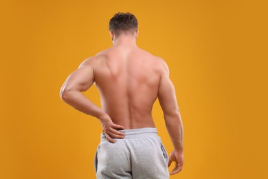 Photo of Man suffering from back pain on orange background, back view