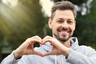 Happy man making heart with hands outdoors