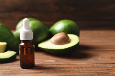 Bottle with oil and fresh avocados on wooden table