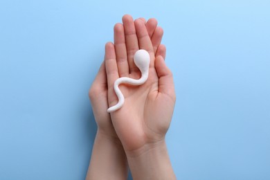 Reproductive medicine. Woman holding figure of sperm cell on light blue background, top view