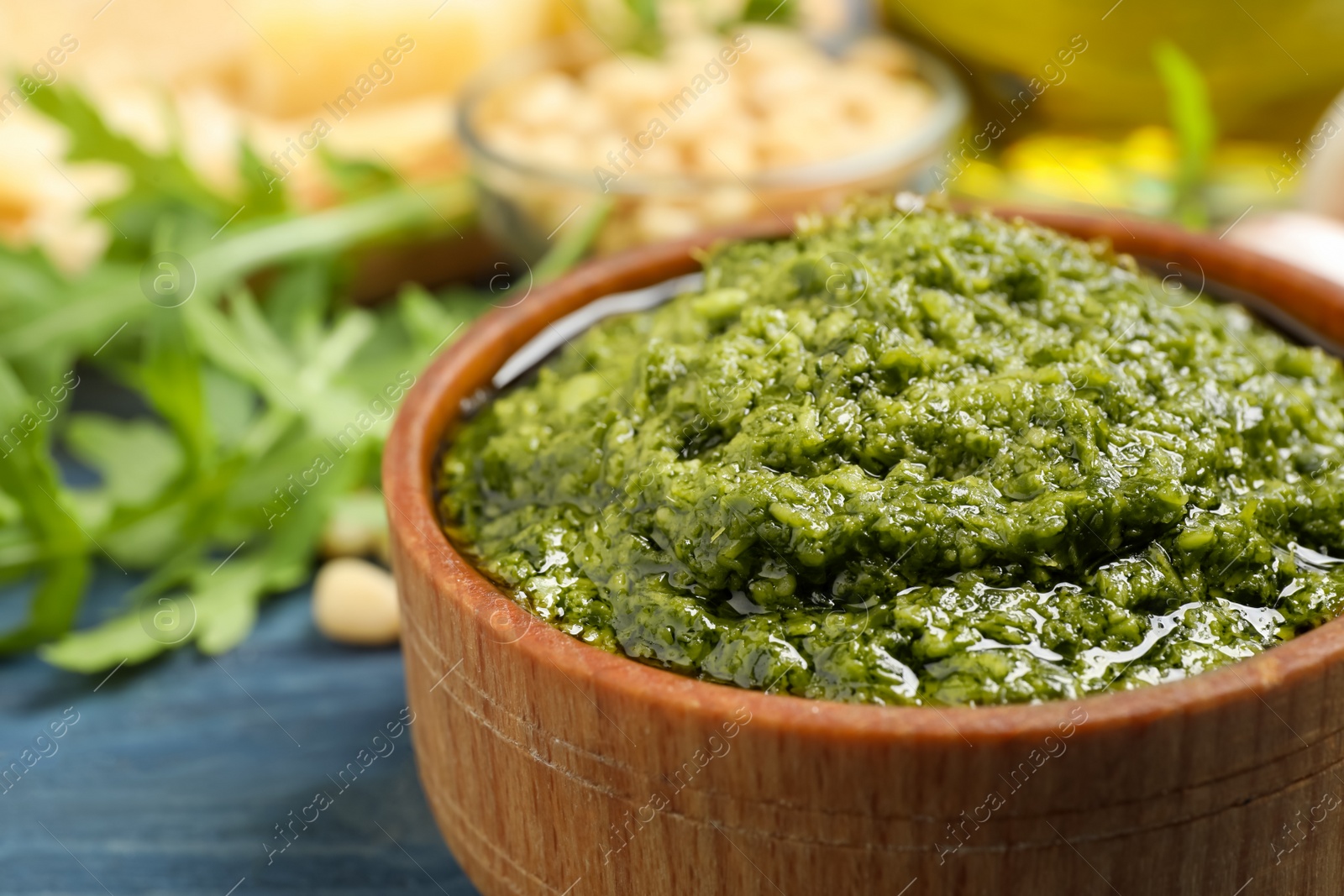 Photo of Bowl of tasty arugula pesto on blue wooden table, closeup