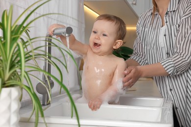 Mother washing her little baby in sink at home