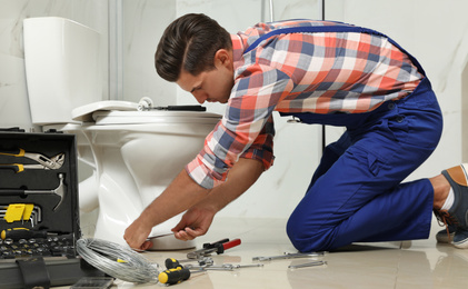 Professional plumber working with toilet bowl in bathroom