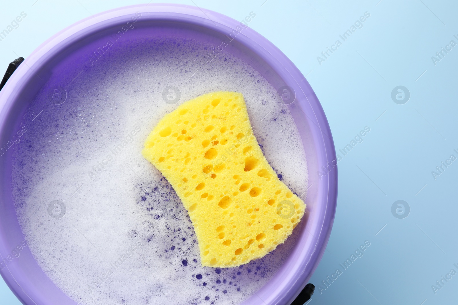 Photo of Bucket with foam and sponge on light blue background, top view