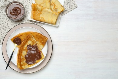 Photo of Tasty crepes with chocolate paste served on white wooden table, flat lay. Space for text