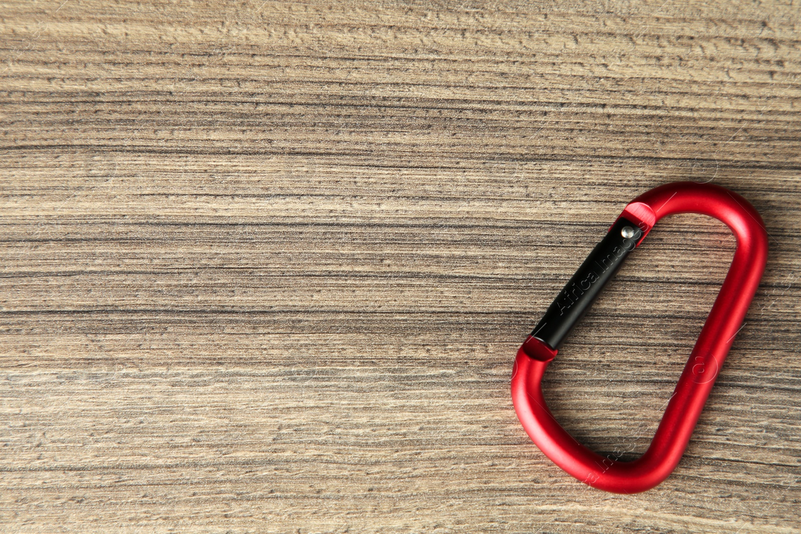 Photo of One metal carabiner on wooden table, top view. Space for text