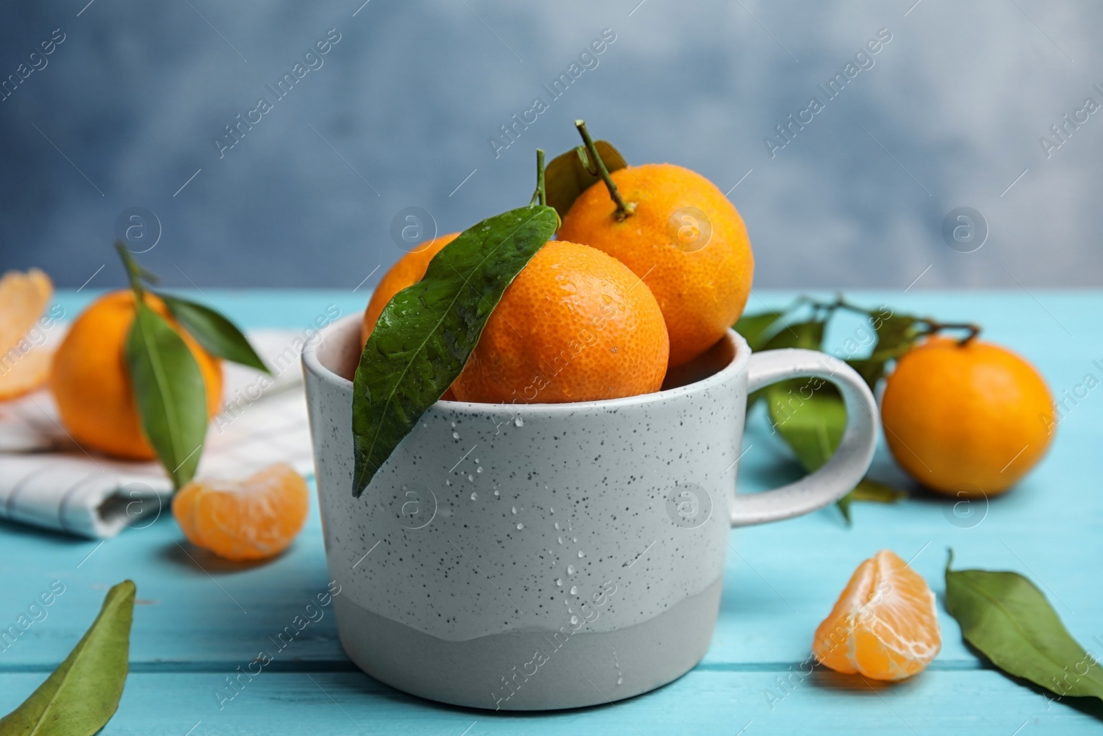 Photo of Fresh ripe tangerines with green leaves and mug on table