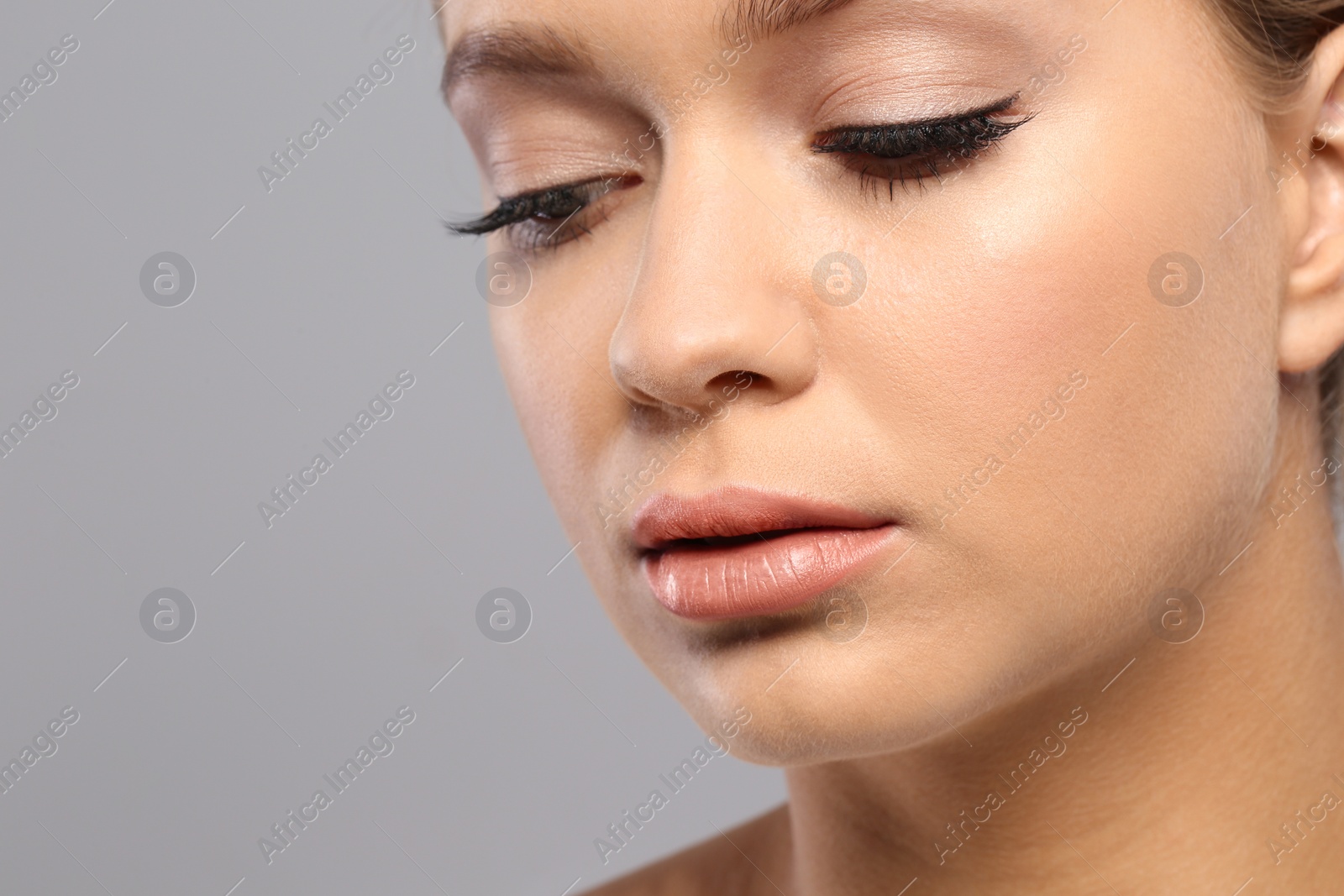 Photo of Young woman wearing nude lipstick on gray background