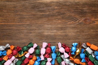 Many candies in colorful wrappers on wooden table, flat lay. Space for text