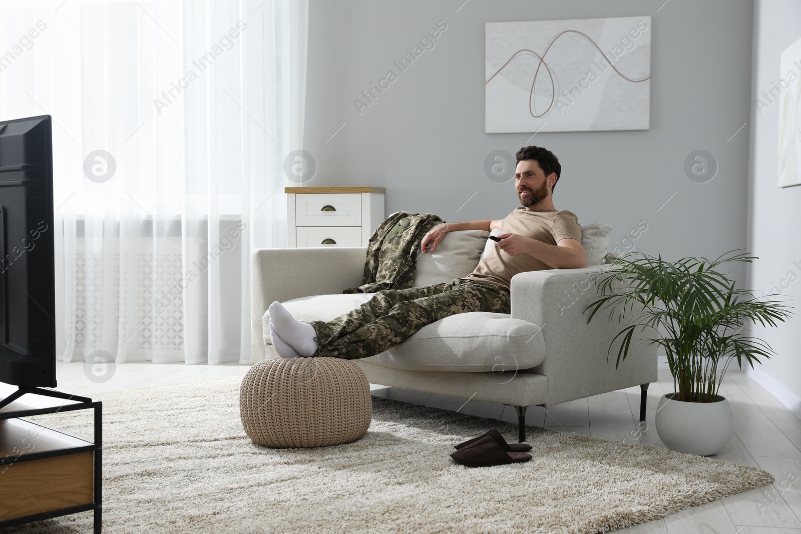 Photo of Happy soldier watching TV on sofa in living room. Military service