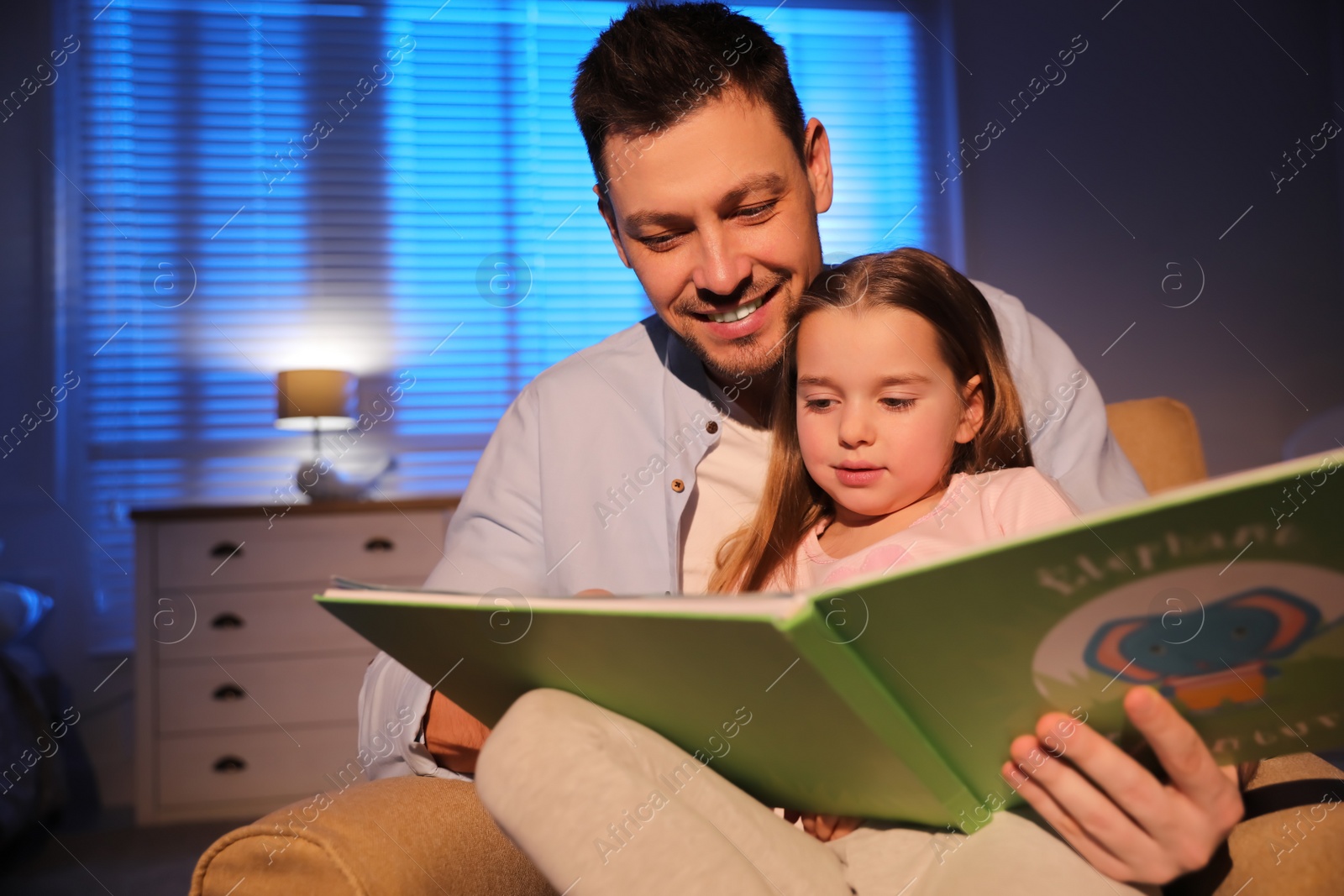 Photo of Father reading bedtime story to his daughter at home