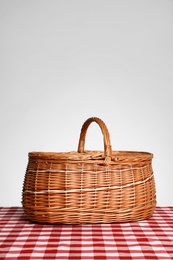 Photo of Closed wicker picnic basket on checkered tablecloth against white background