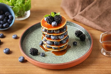 Tasty pancakes with berries and syrup on plate