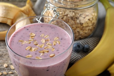 Photo of Glass of tasty banana blueberry smoothie with oatmeal on table, closeup