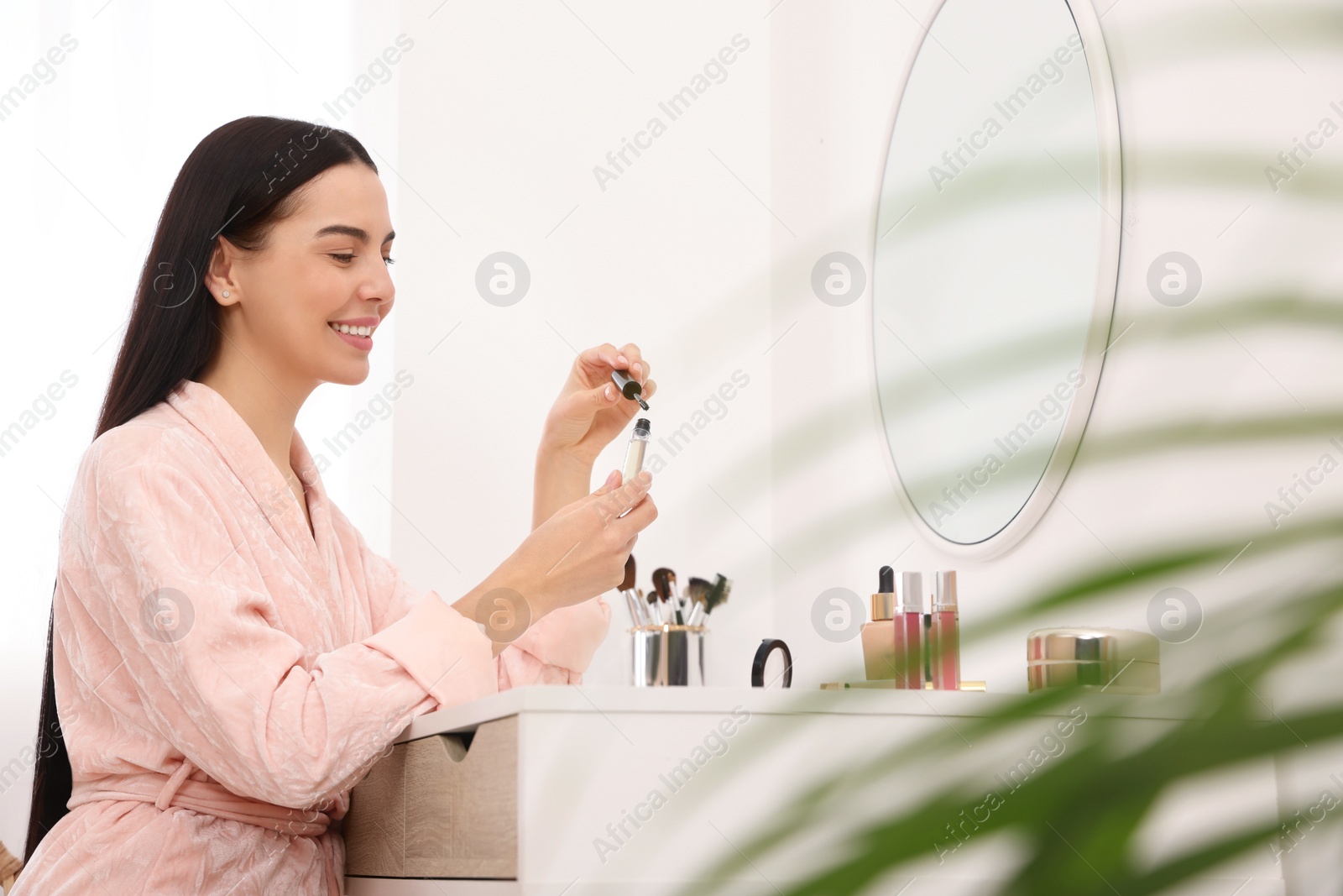 Photo of Beautiful young woman with gel for eyelashes at dressing table indoors