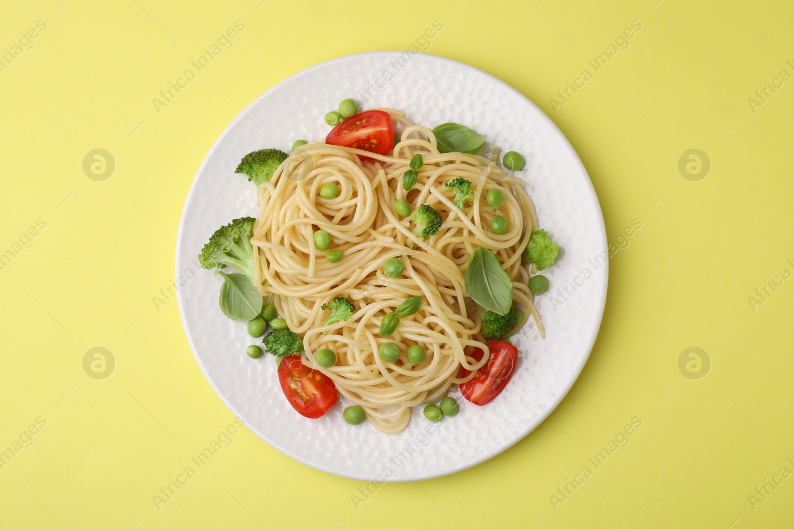 Photo of Plate of delicious pasta primavera on yellow background, top view