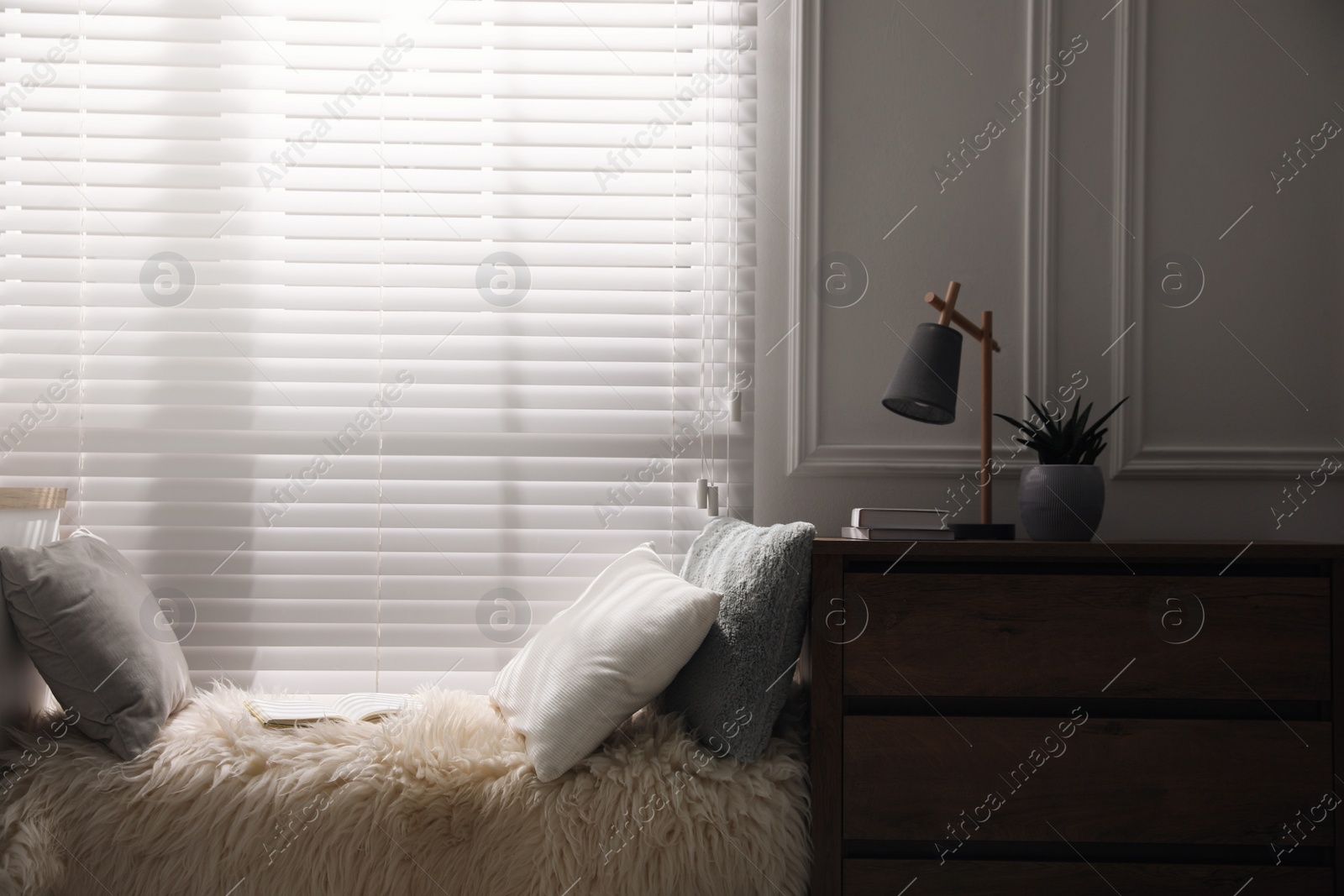 Photo of Comfortable place for relax with faux fur and pillows near window in room