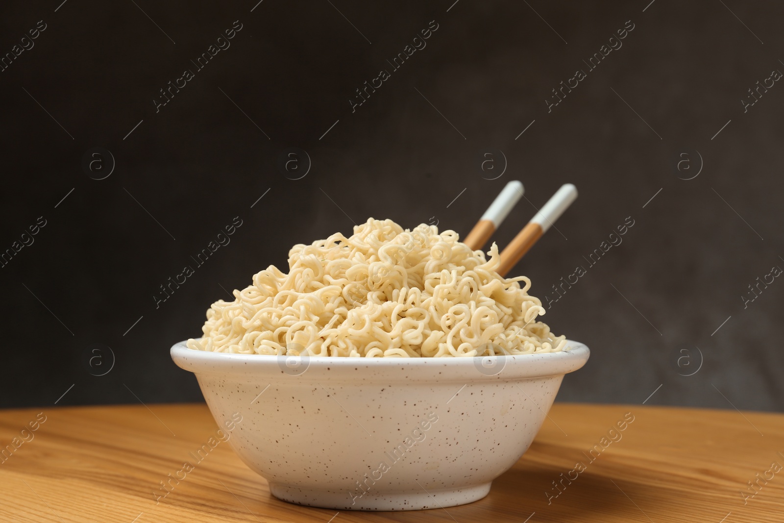 Photo of Bowl of hot noodles with chopsticks on table against grey background