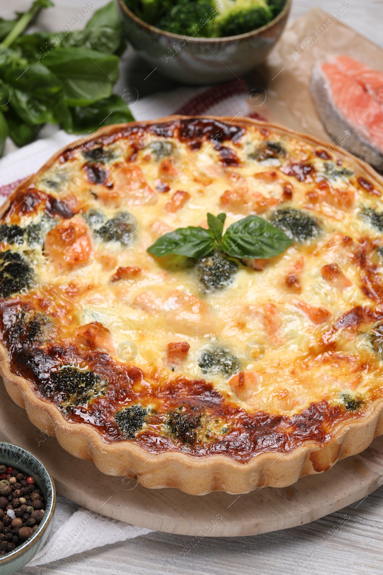 Photo of Delicious homemade quiche with salmon, broccoli and basil leaves on table