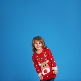 Photo of Cute little girl in red Christmas sweater smiling against blue background