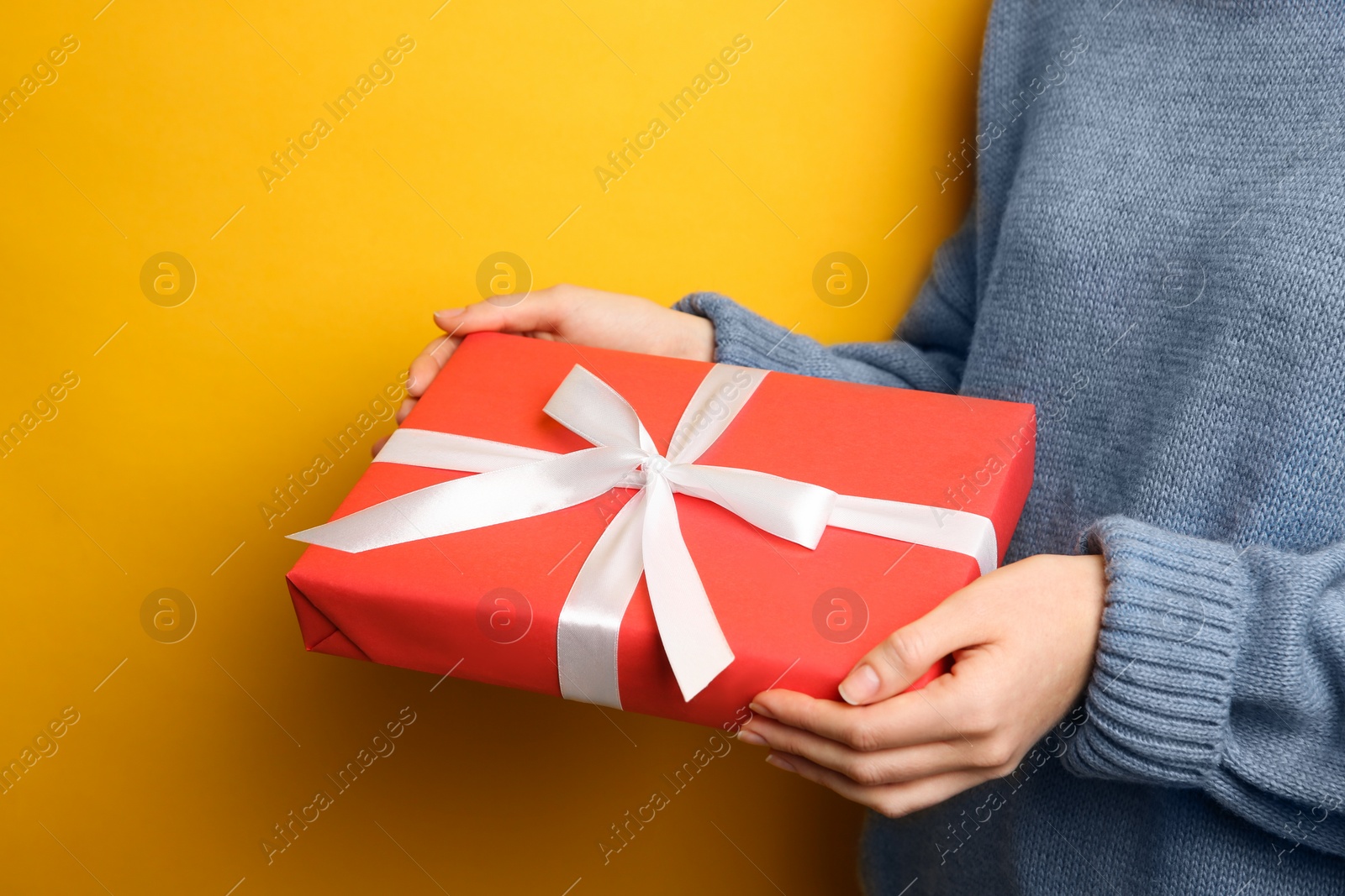 Photo of Woman holding Christmas gift box on yellow background, closeup