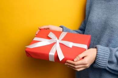 Woman holding Christmas gift box on yellow background, closeup