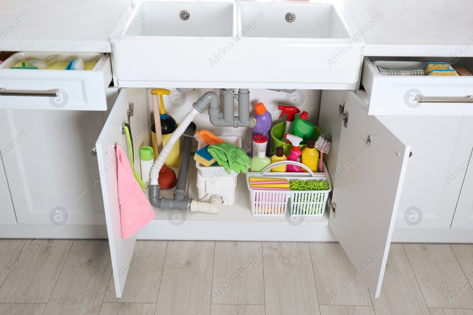 Photo of Open under sink cabinet with different cleaning supplies in kitchen