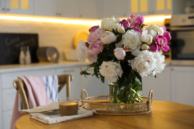 Photo of Beautiful peonies and cup of coffee on wooden table in kitchen