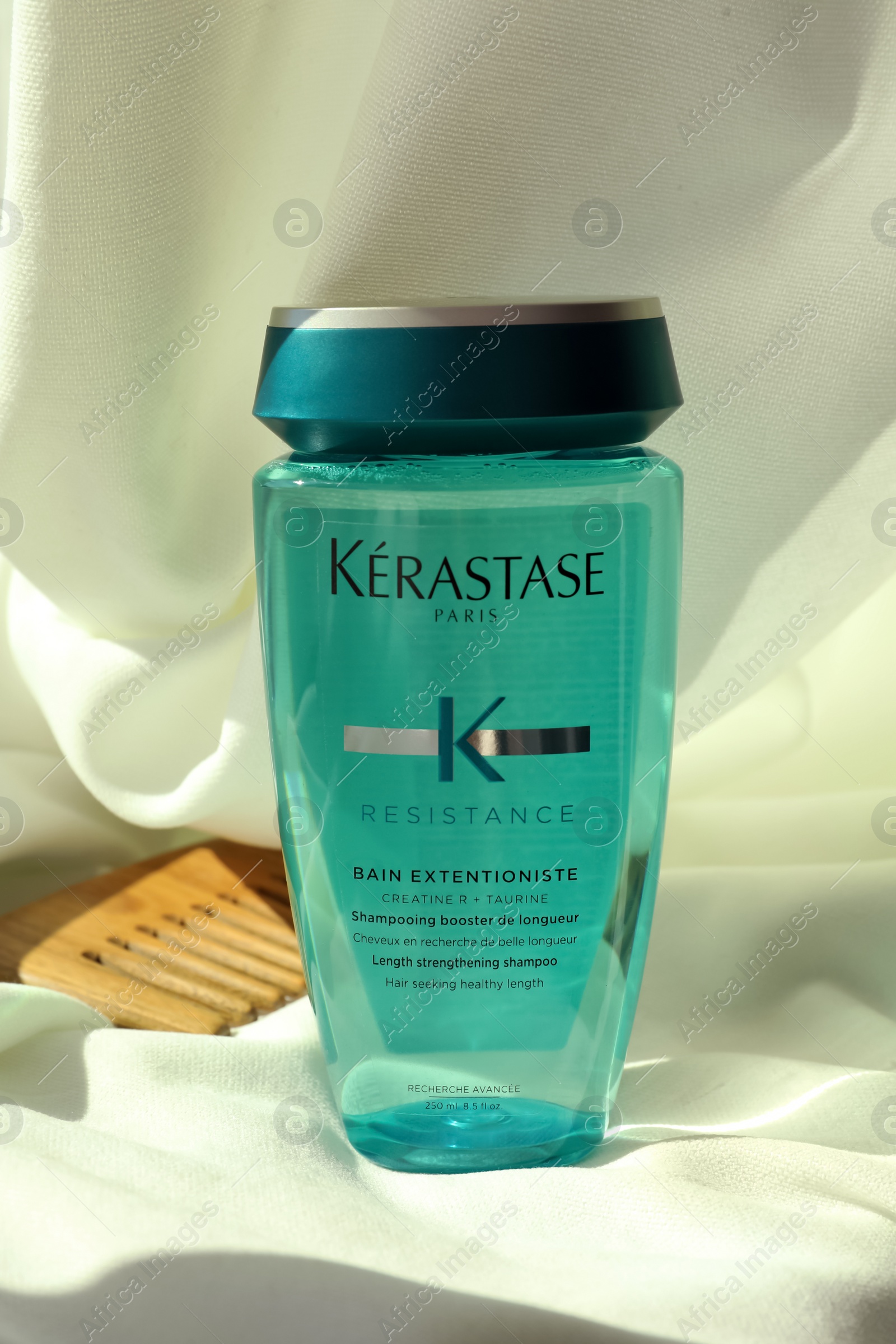 Photo of MYKOLAIV, UKRAINE - SEPTEMBER 07, 2021: Kerastase shampoo and wooden comb on white fabric. Hair care cosmetic product