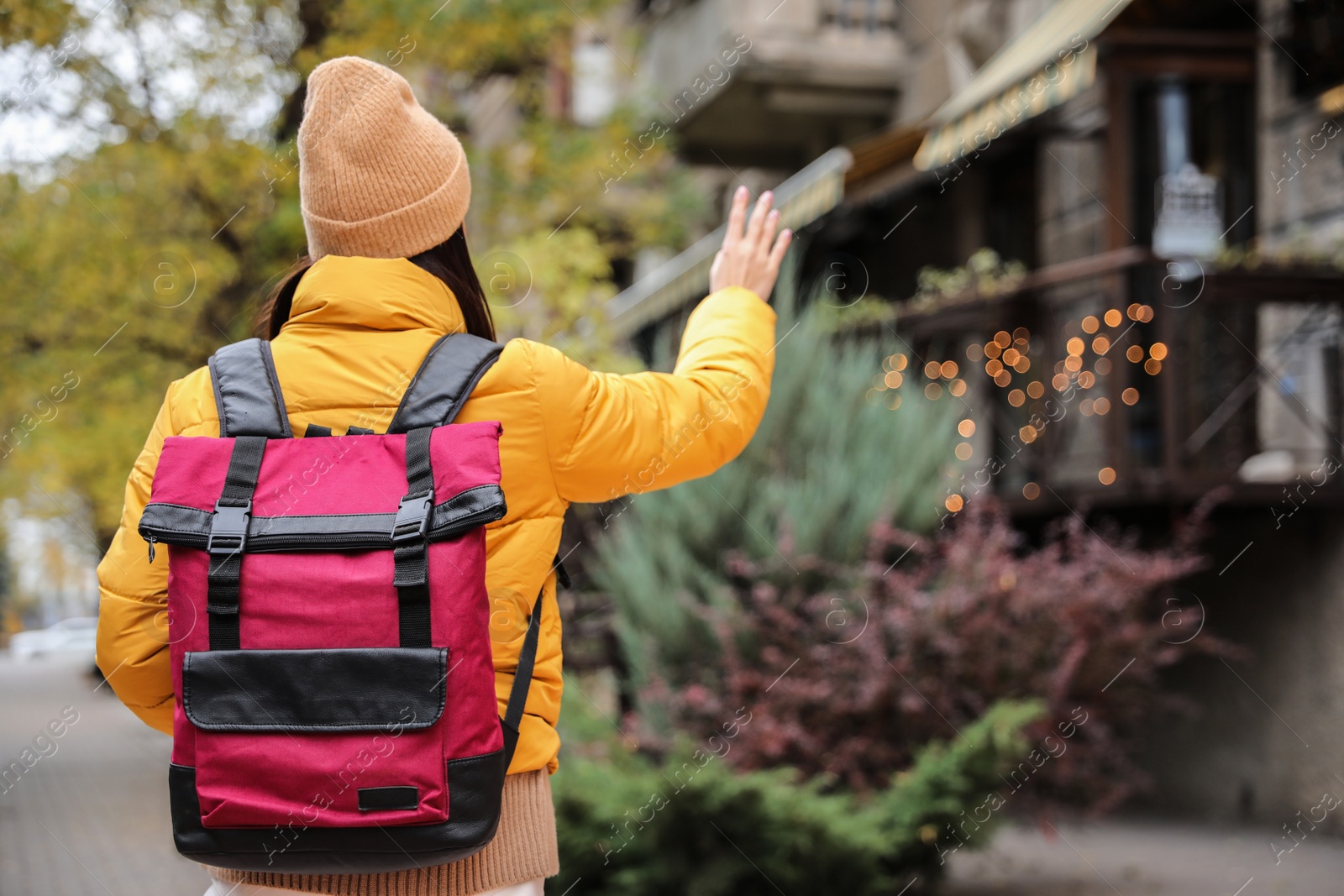 Photo of Female tourist with travel backpack on city street, back view. Urban trip