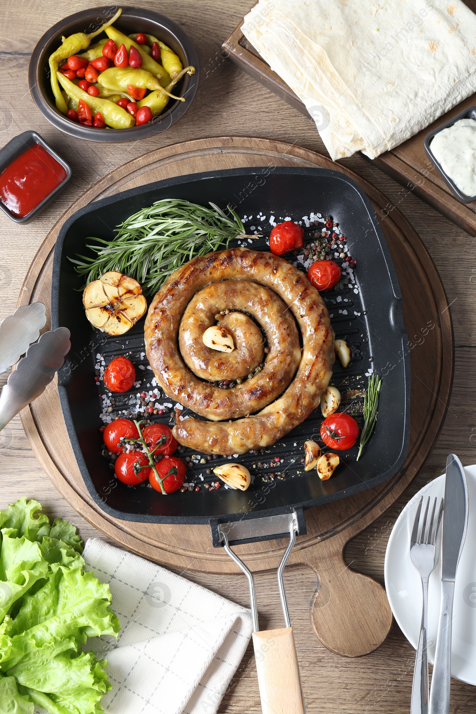 Photo of Delicious homemade sausage with garlic, tomatoes, rosemary and spices served on wooden table, flat lay