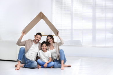 Happy family sitting under cardboard roof at home. Insurance concept