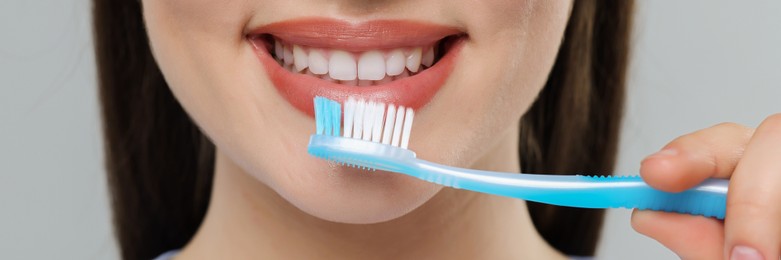 Woman brushing her teeth with plastic toothbrush on light grey background, closeup. Banner design