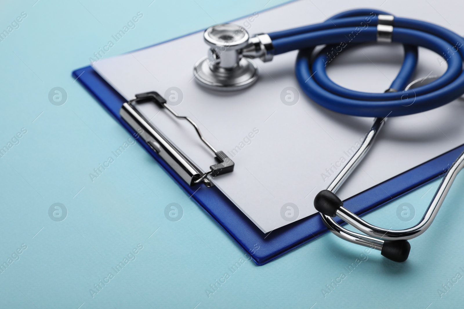 Photo of Clipboard with stethoscope on turquoise background, closeup. Space for text