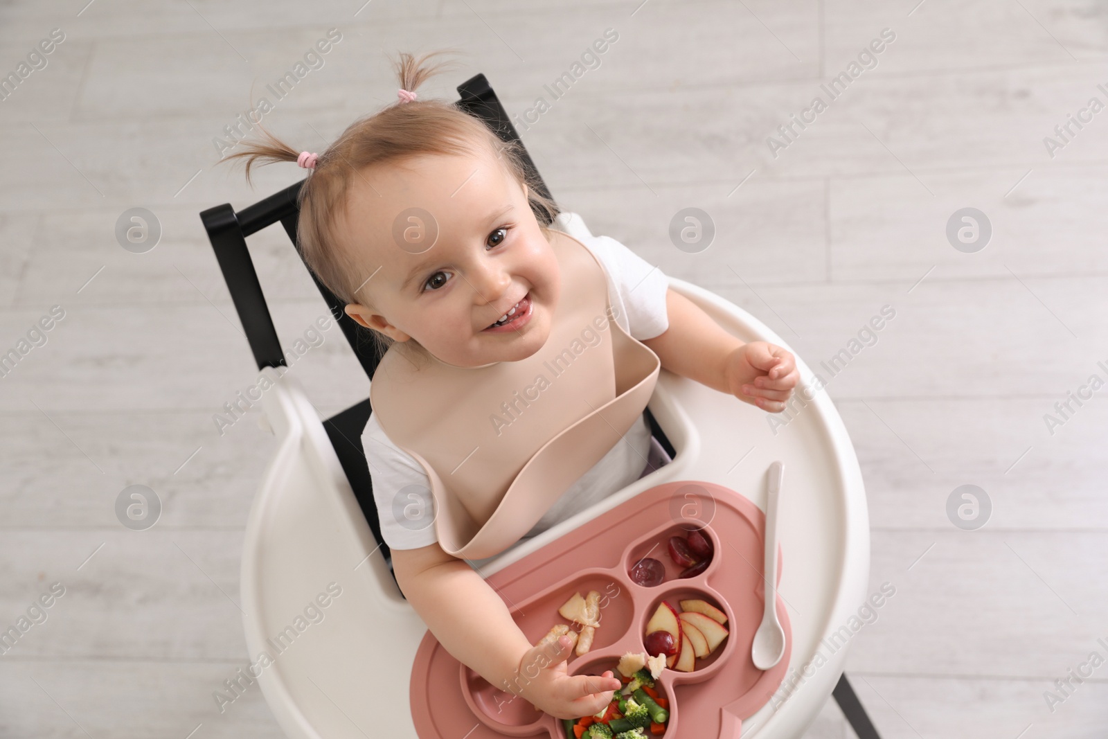 Photo of Cute little baby eating food in high chair indoors, above view