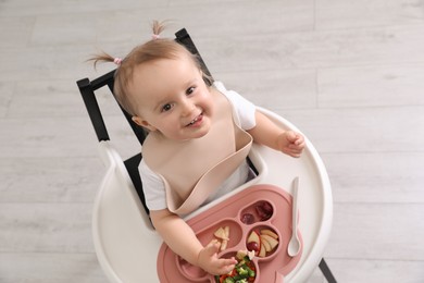 Photo of Cute little baby eating food in high chair indoors, above view