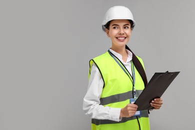 Engineer in hard hat holding clipboard on grey background, space for text