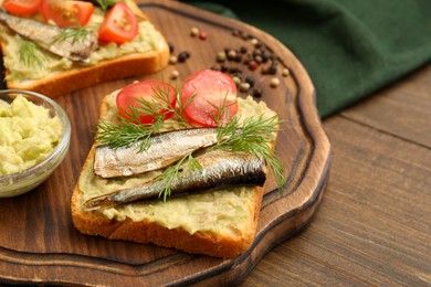 Photo of Delicious sandwich with sprats, tomato, dill and avocado puree on wooden table, closeup. Space for text