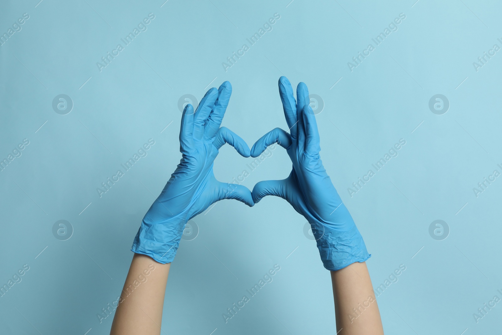 Photo of Doctor in medical gloves making heart with hands on light blue background, closeup