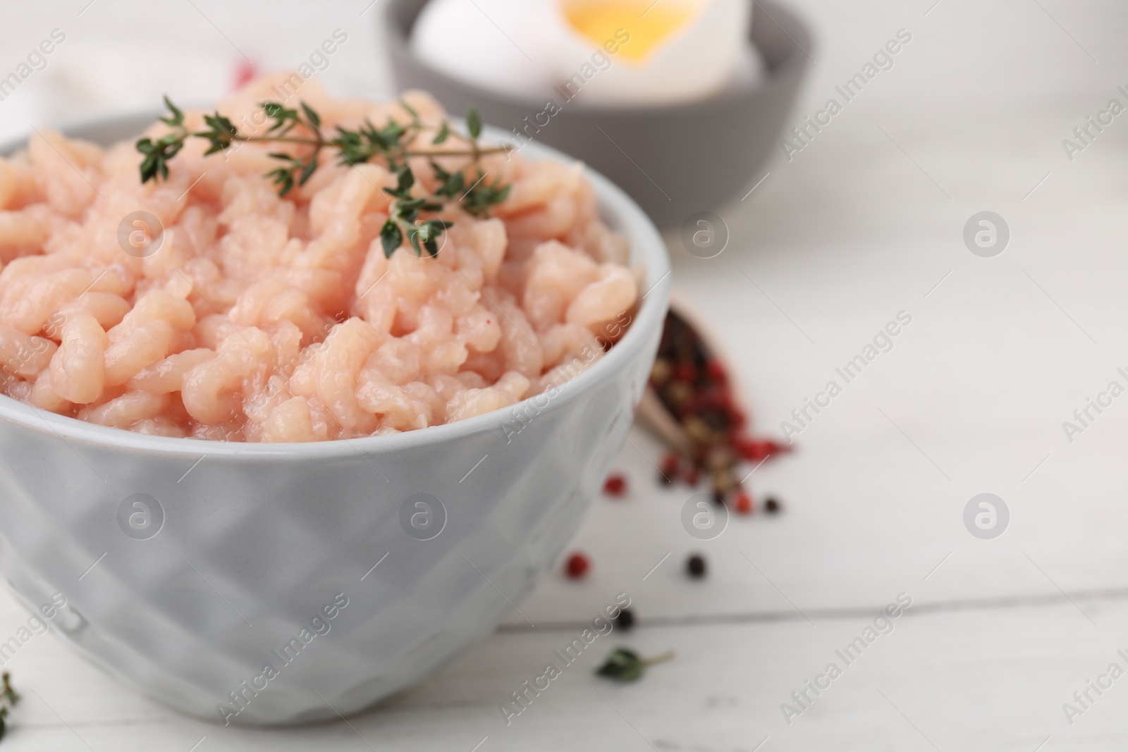 Photo of Fresh raw minced meat and thyme in bowl on white wooden table, closeup. Space for text