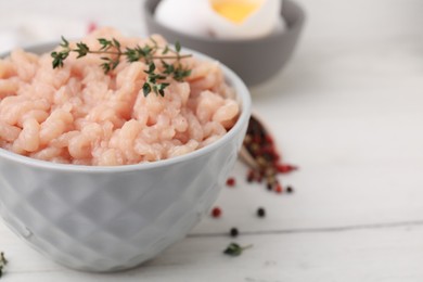 Photo of Fresh raw minced meat and thyme in bowl on white wooden table, closeup. Space for text