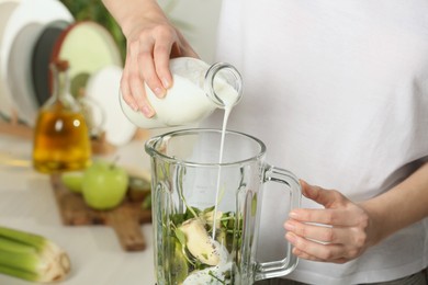 Photo of Woman adding milk into blender with ingredients for green smoothie, closeup